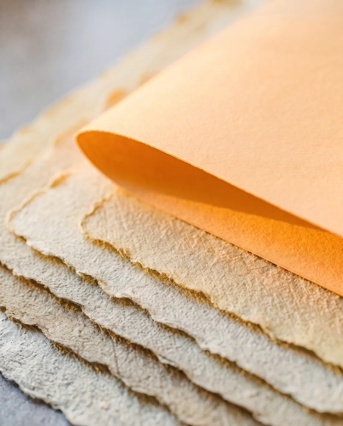 Vergilbte Lagen aus handgeschöpftem Büttenpapier, darüber eine neue, glatte Papierlage im warmen Morgenlicht